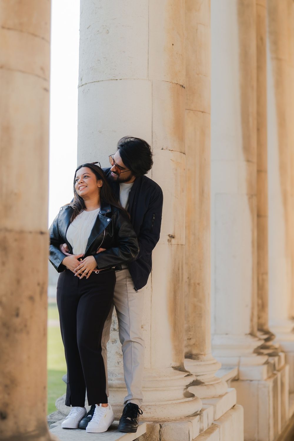 Couple in black leather jackets sharing a romantic moment between white columns of a classical building.