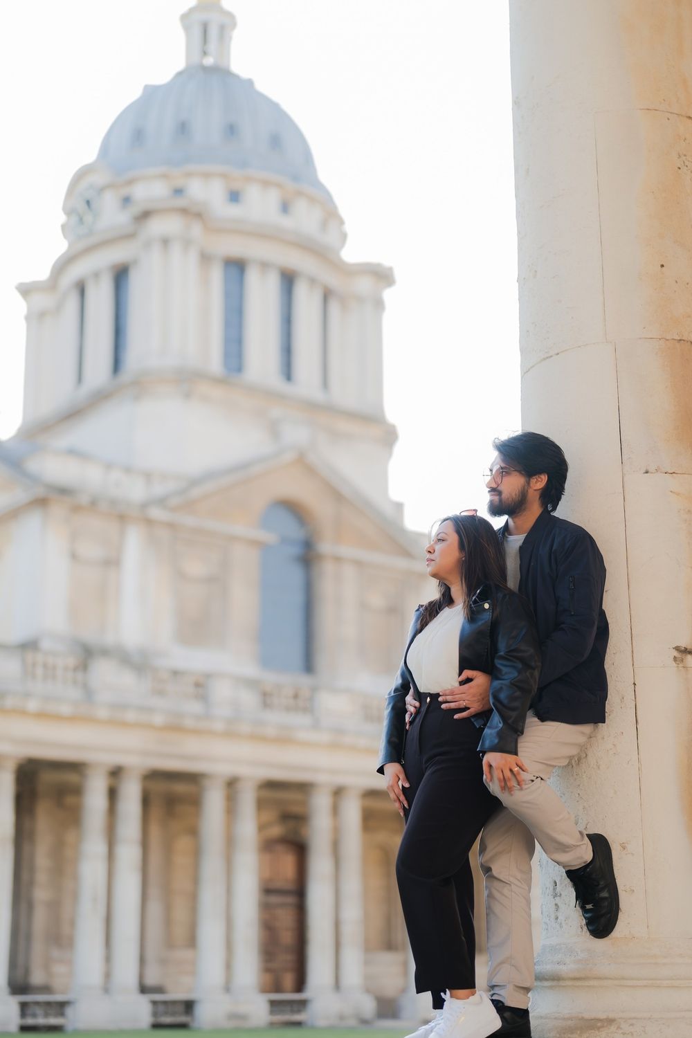 Couple posing by a column at the Old Royal Naval College in Greenwich, London, with the iconic dome in the background.