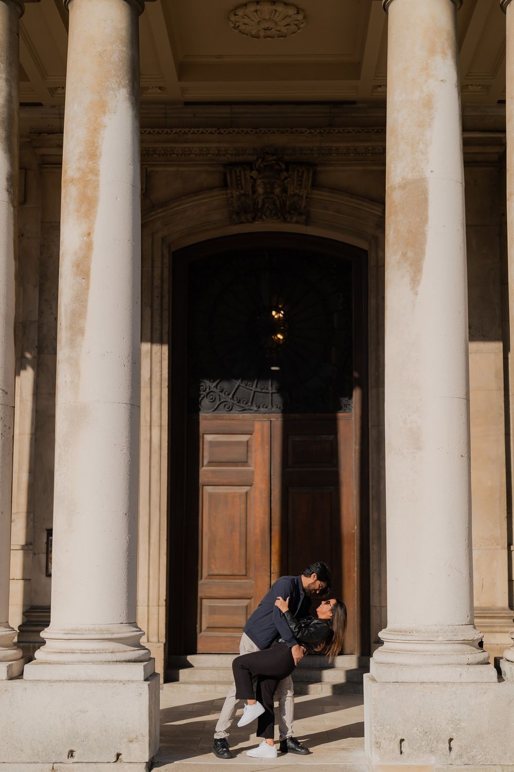 Couple sharing a romantic moment on steps between grand columns of a classical building with ornate wooden door.