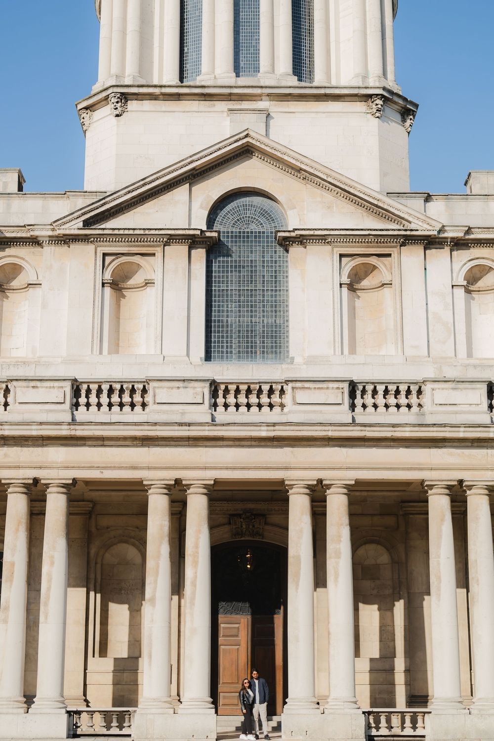 Couple standing at the entrance of a grand neoclassical building with tall columns and ornate facade.