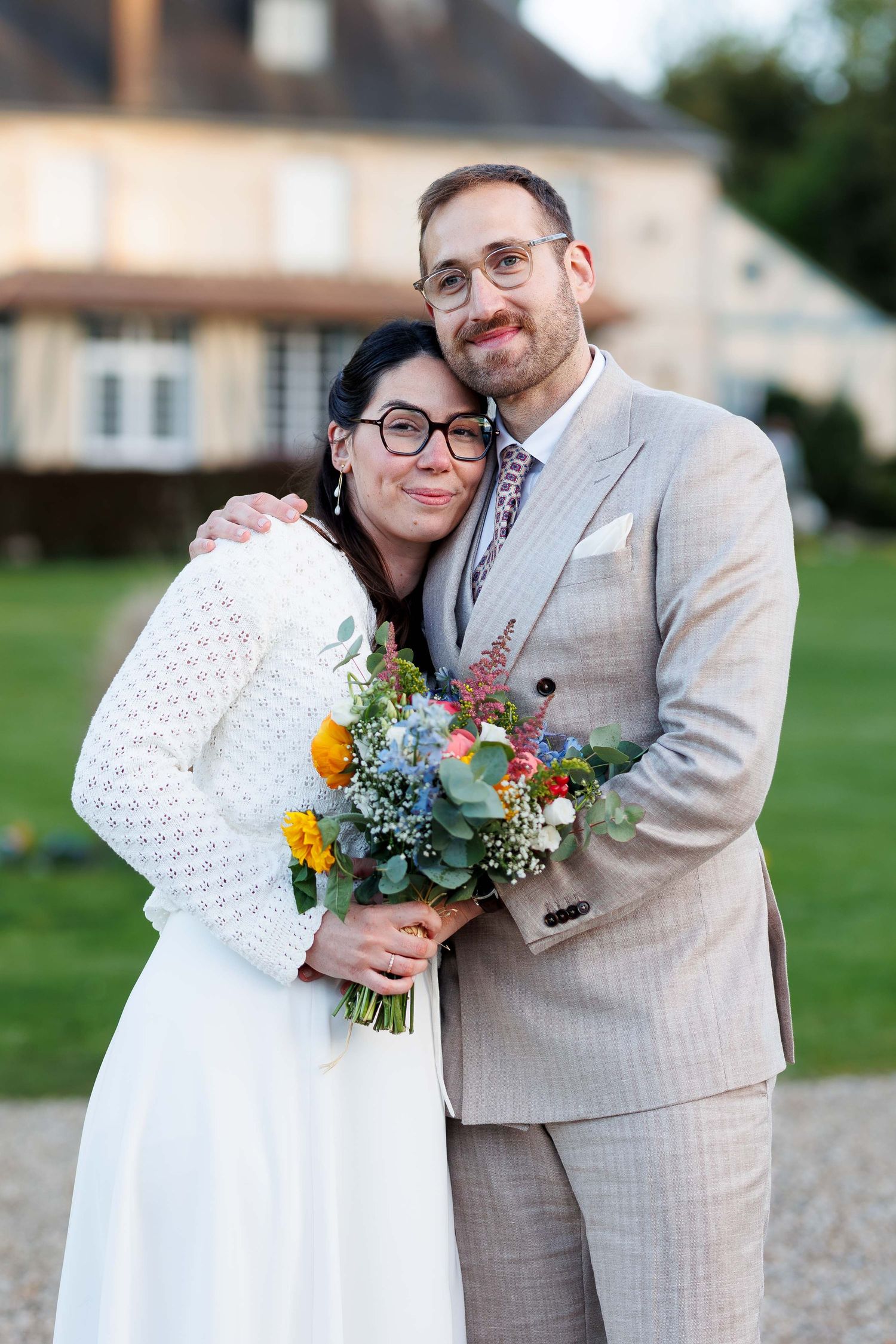 A smiling couple in wedding attire reads a personalized French newspaper together outdoors.