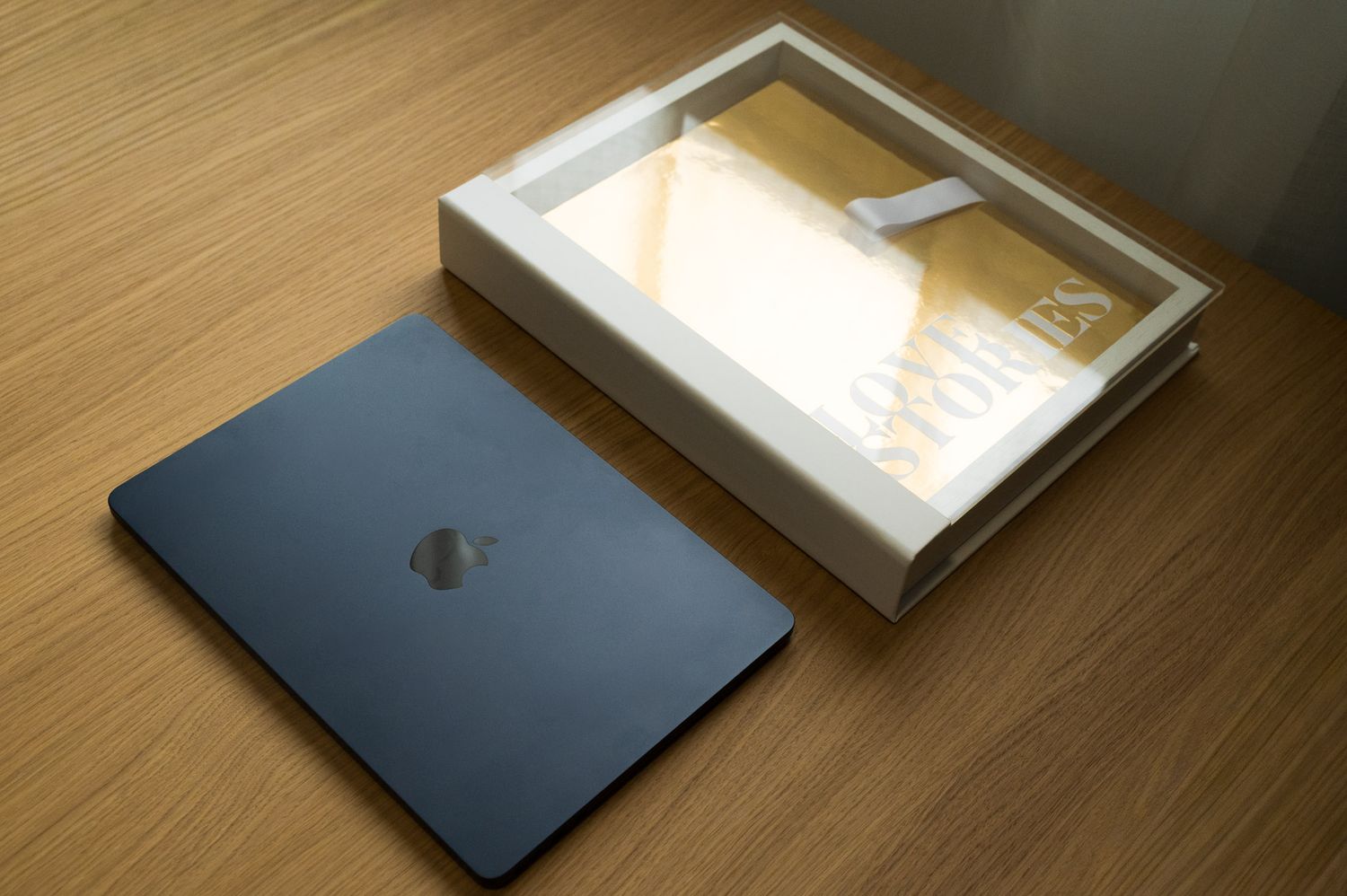 Love Stories gold metallic photo book beside its open white acrylic display case on wood desk.