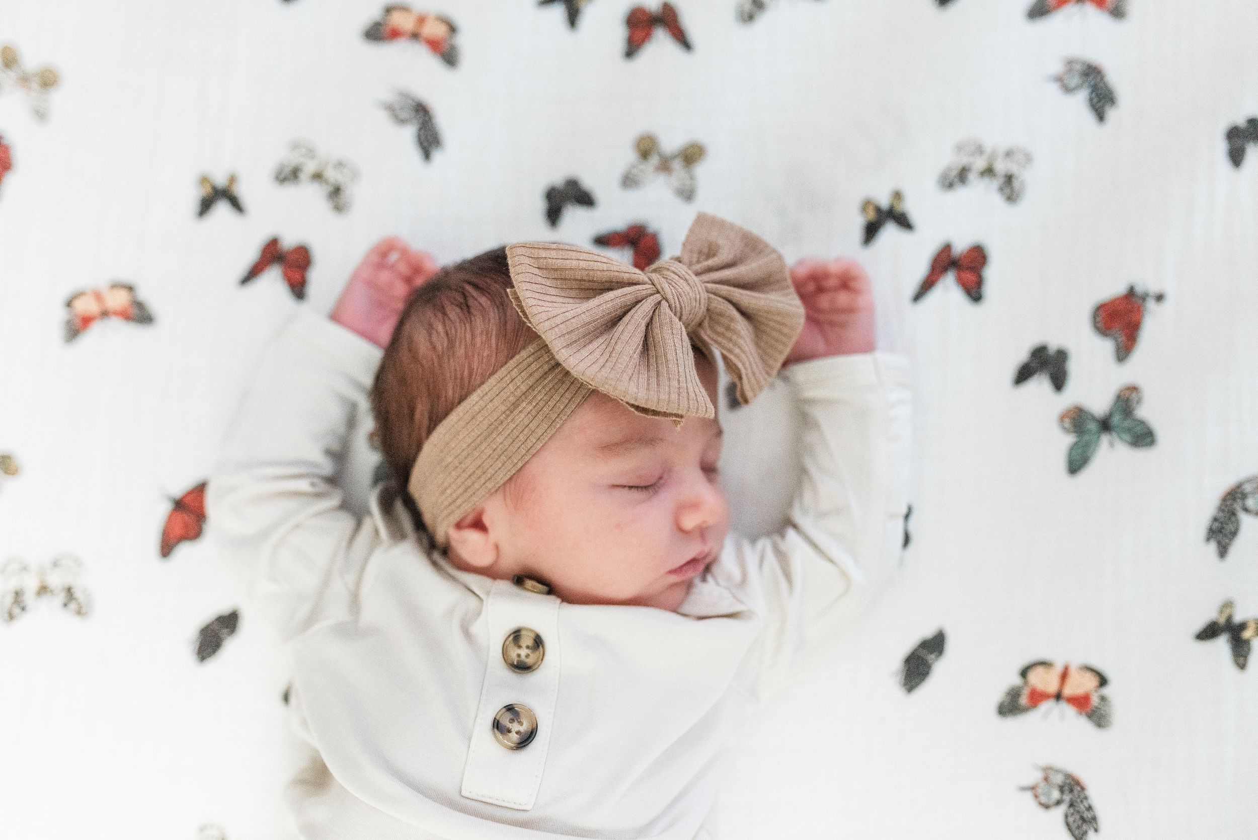 Sleeping baby in white clothing surrounded by colorful butterfly decorations on white background.