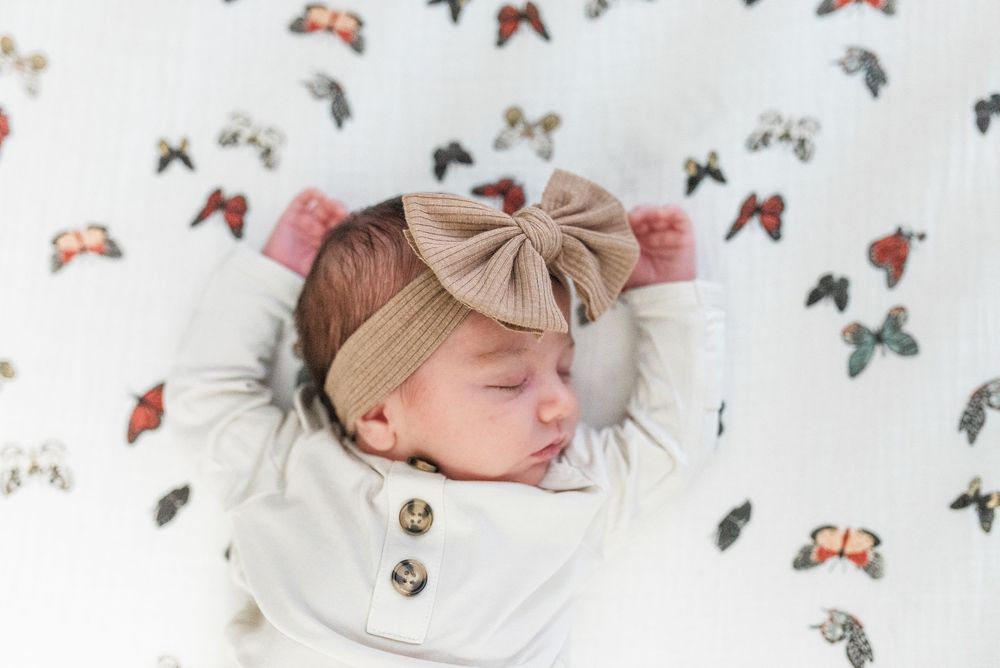 Sleeping baby in white clothing surrounded by colorful butterfly decorations on white background.