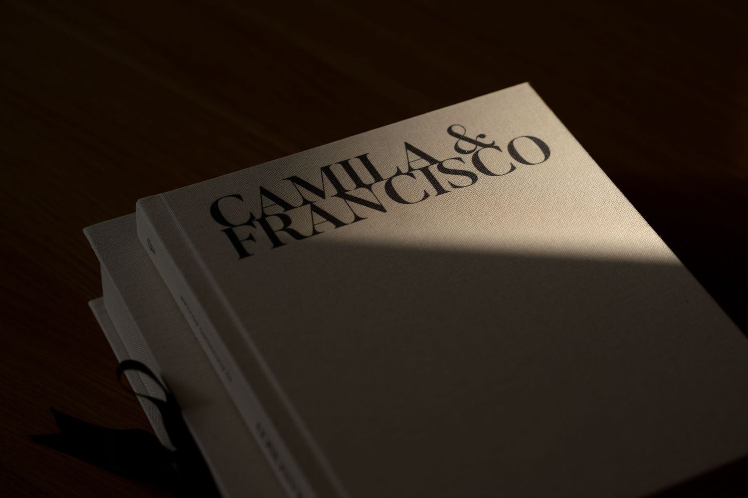 Elegant hardcover wedding photo book with embossed names Camila and Francisco on a dark wooden surface.