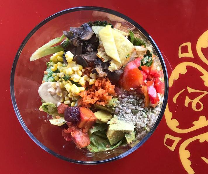 Colorful healthy salad bowl with avocado, tomatoes, corn, carrots, and mixed greens served in a glass bowl.