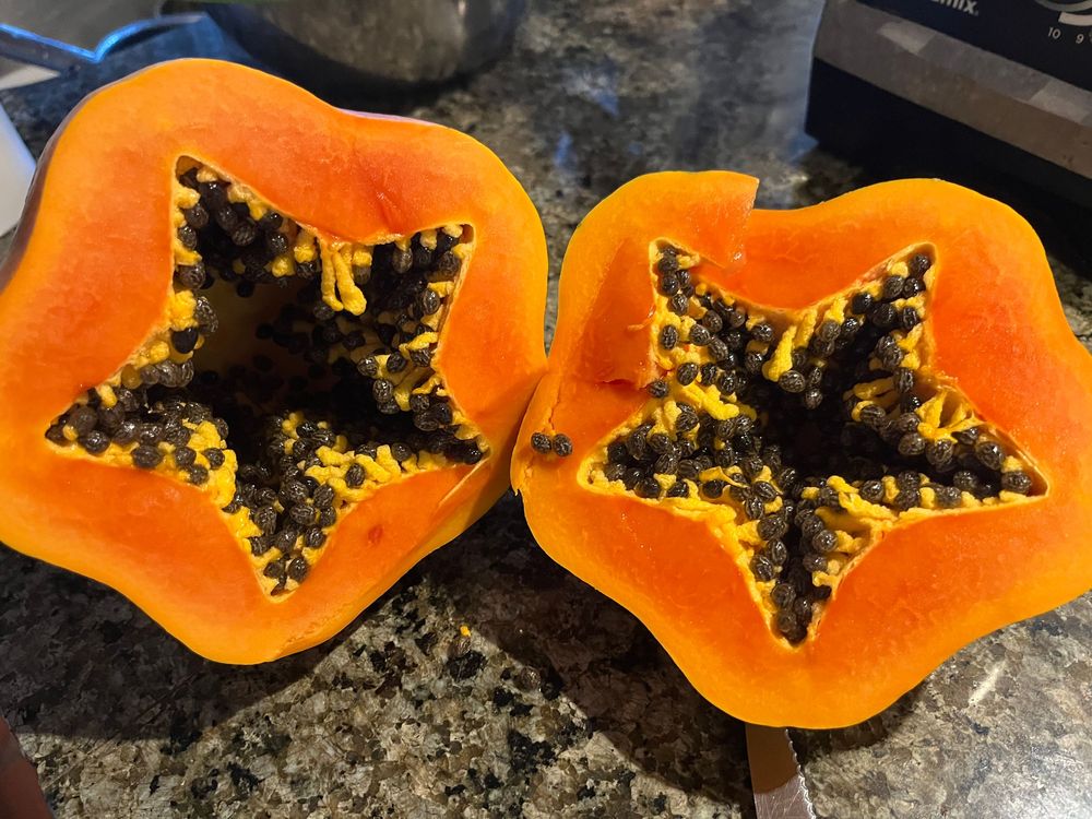 Two halves of a ripe papaya with black seeds on a granite countertop.