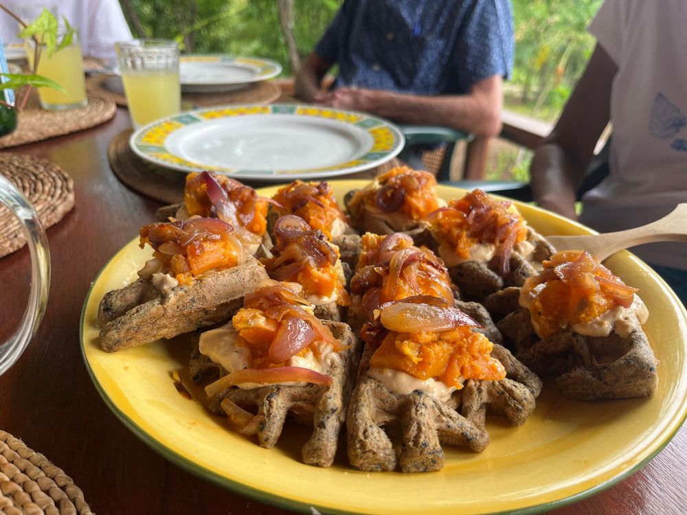 Savory dark waffles topped with orange sauce and shrimp served on a yellow plate at an outdoor restaurant.