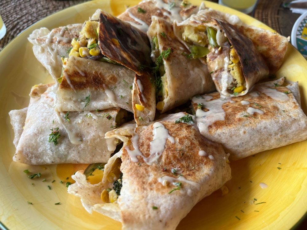 Golden-brown grilled burritos sliced and served on a yellow plate, filled with corn, greens, and melted cheese.