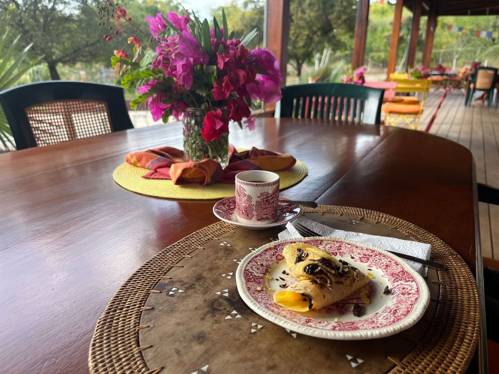 Elegant breakfast table with eggs Benedict, coffee, fresh bougainvillea flowers, and pastries on a wooden dining table.