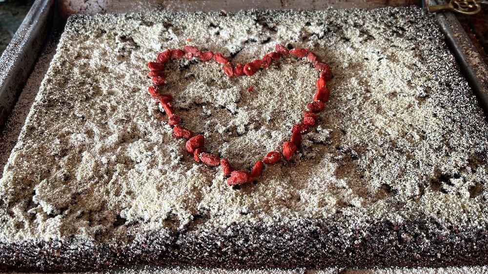 Heart shape made of red berries on a chocolate cake dusted with powdered sugar in a baking pan.