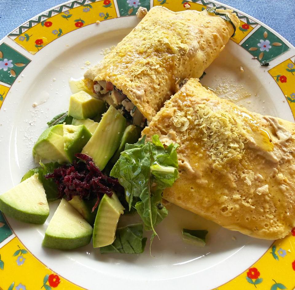 Golden omelette stuffed with filling, served with fresh avocado salad and mixed greens on a colorful floral plate.