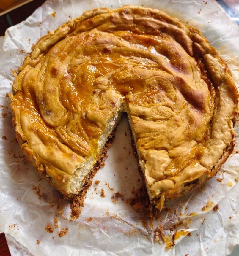Golden-crusted pie with a slice removed, revealing a creamy filling, resting on parchment paper.
