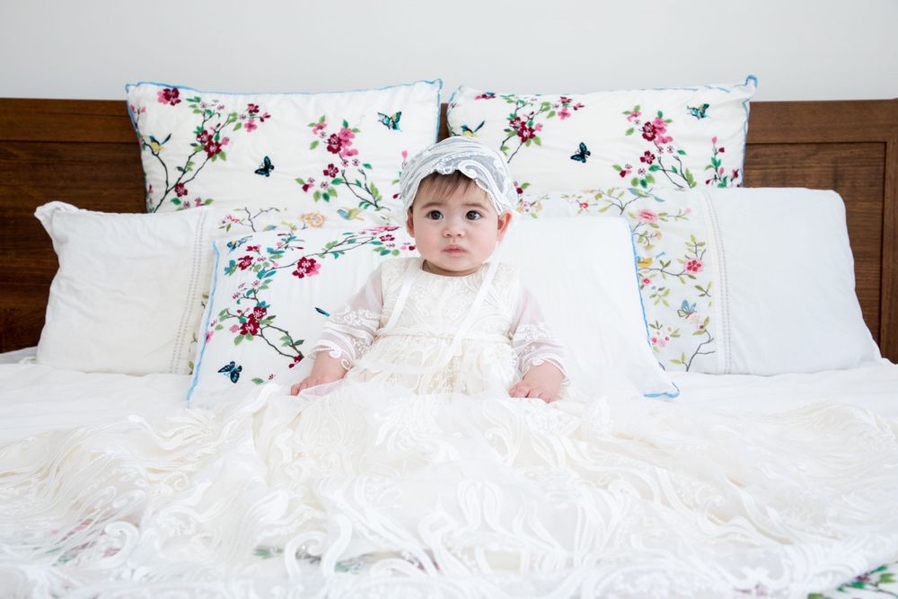 baby on christening on bed wearing christening gown