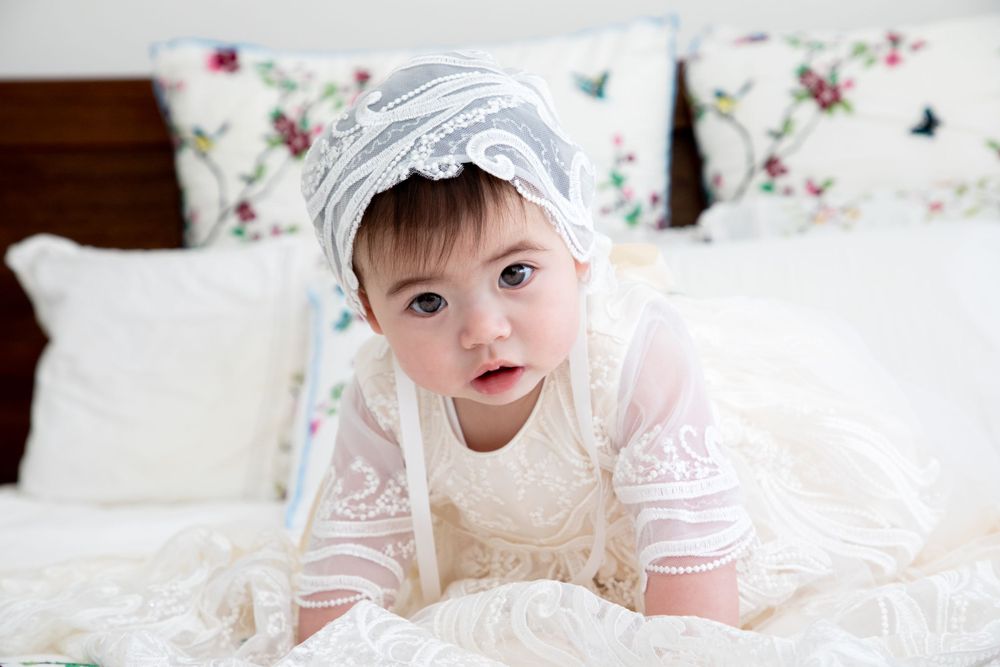 baby on christening on bed wearing christening gown