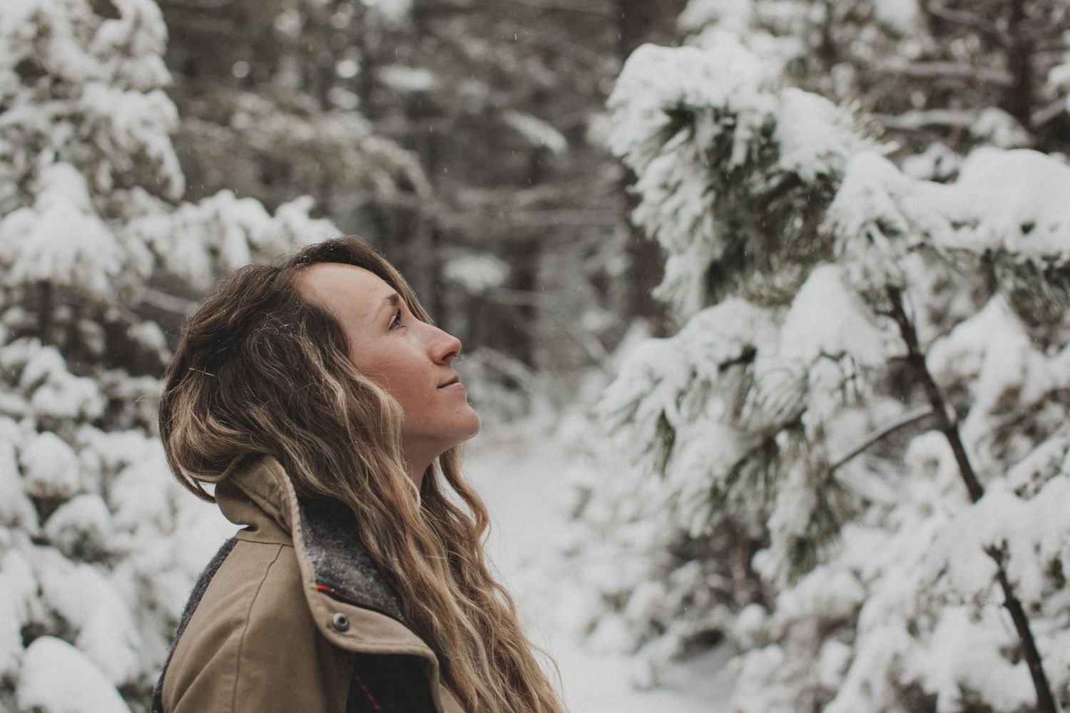 Person enjoying snowfall in winter forest with eyes closed and snow-covered trees.