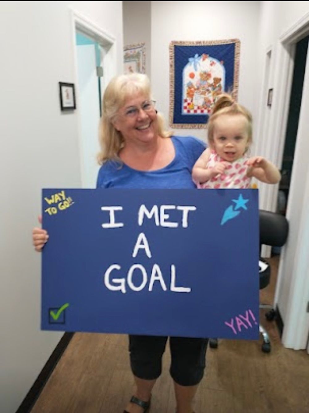 A celebratory moment captured showing an adult and child holding a blue sign that reads 'I MET A GOAL' with decorative details.