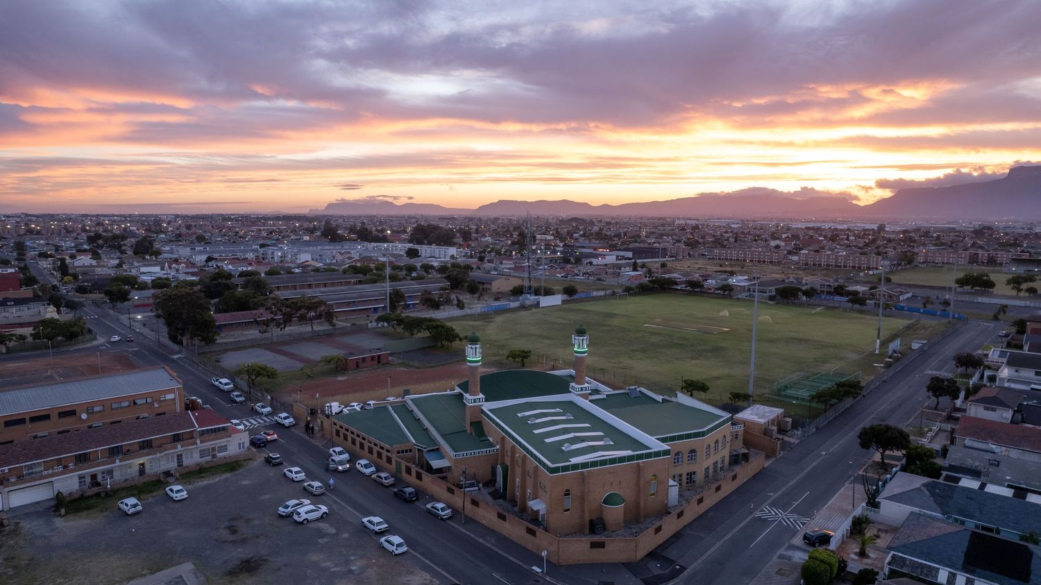 Mosque with green sports field at sunset casting golden light across an urban neighborhood.