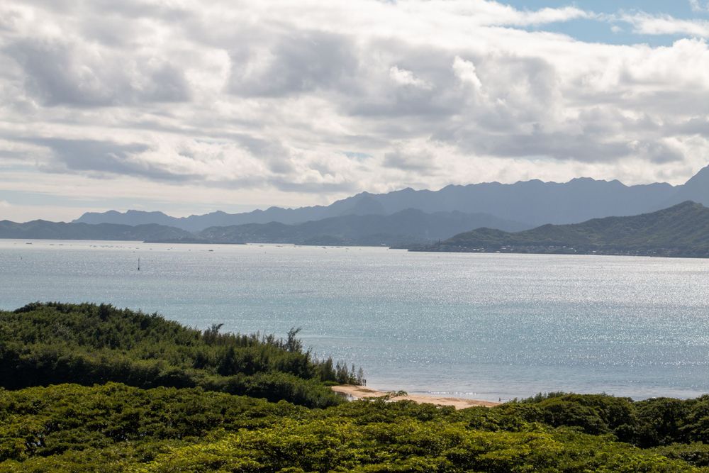 Scenic coastal landscape with mountains, cloudy sky, and turquoise water against a lush green shoreline.