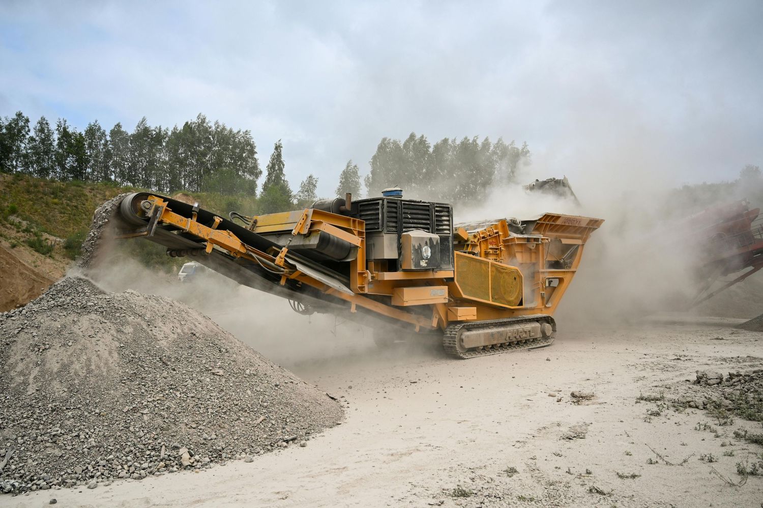 Mobile rock crusher machine processing stone into gravel at quarry site.