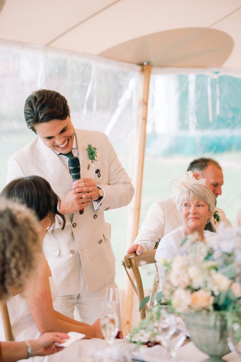 Wedding reception speech under white tent with floral centerpieces and laughing guests at the Lightfoot & Wolfville wedding venue
