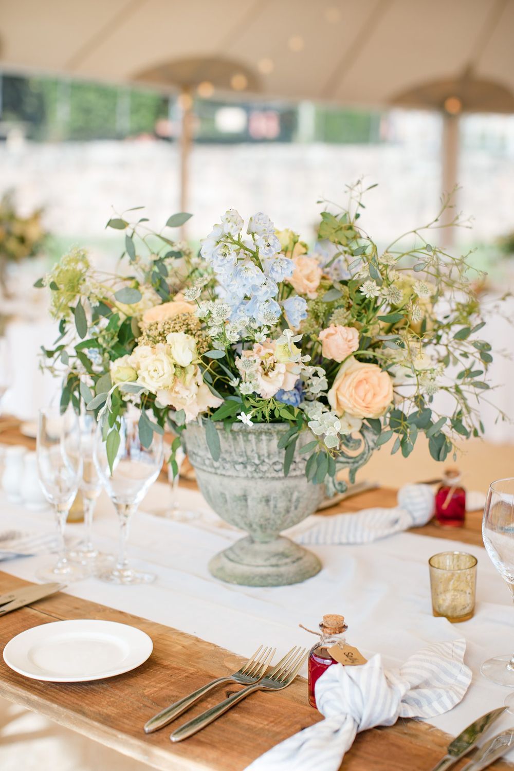 Elegant wedding centerpiece with pastel flowers and greenery in stone urn on white tablecloth inside a tent at the Lightfoot & Wolfville.