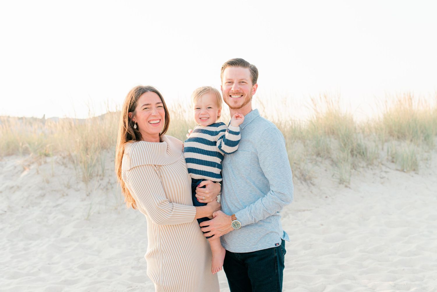 Candid moment of a family laughing together on a Monmouth County beach, with soft fall light and dunes in the background.