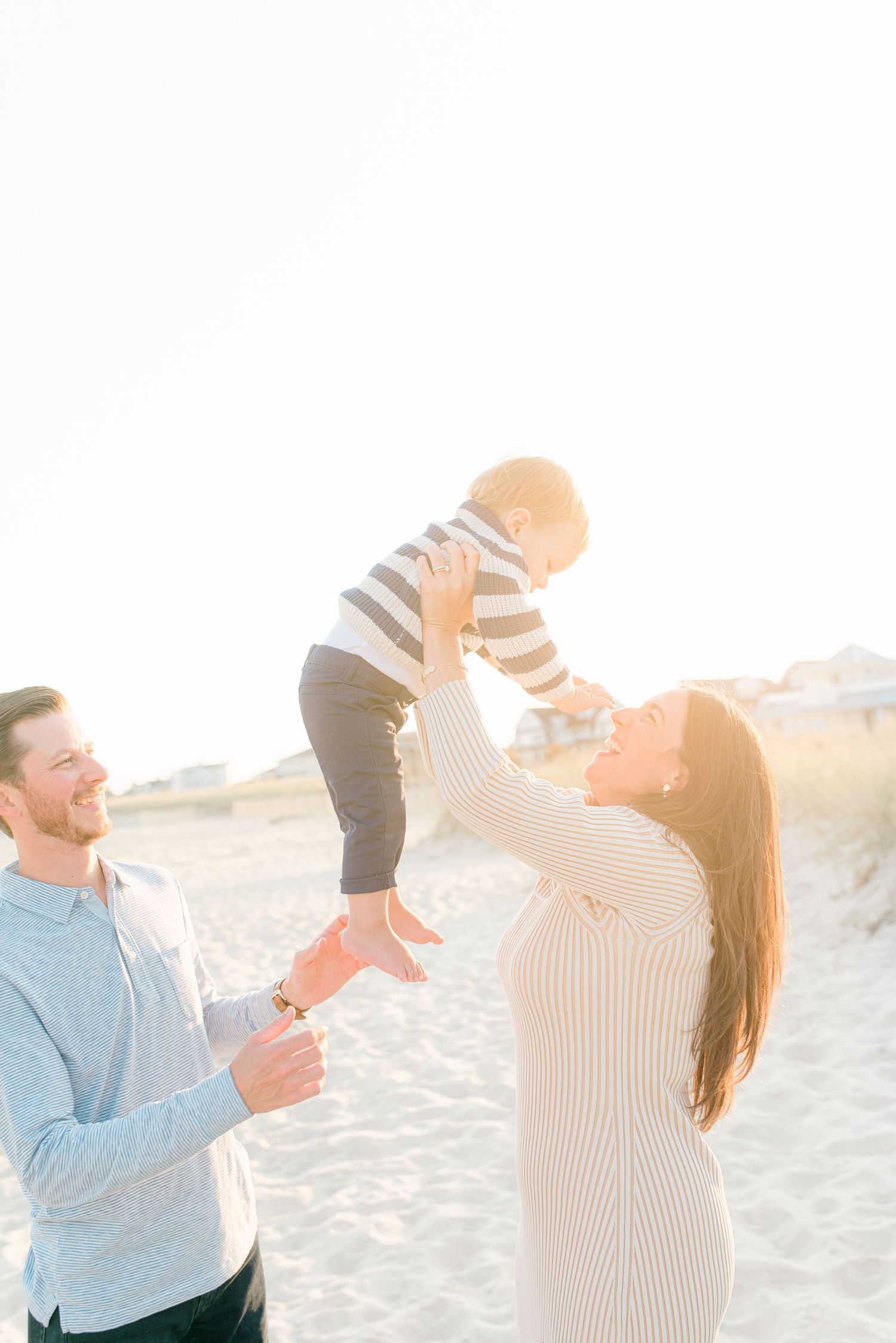 Candid moment of a family laughing together on spring lake beach, with dunes in the background.