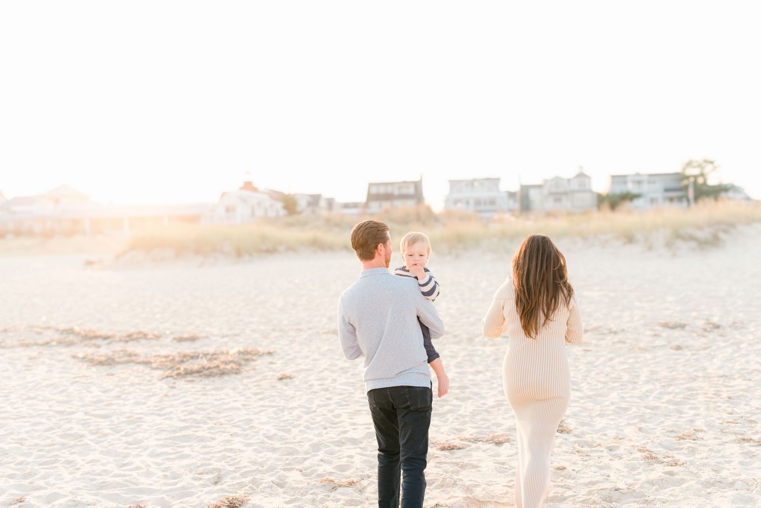 A family walks into the sunset on the spring lake beach during a family photo session.
