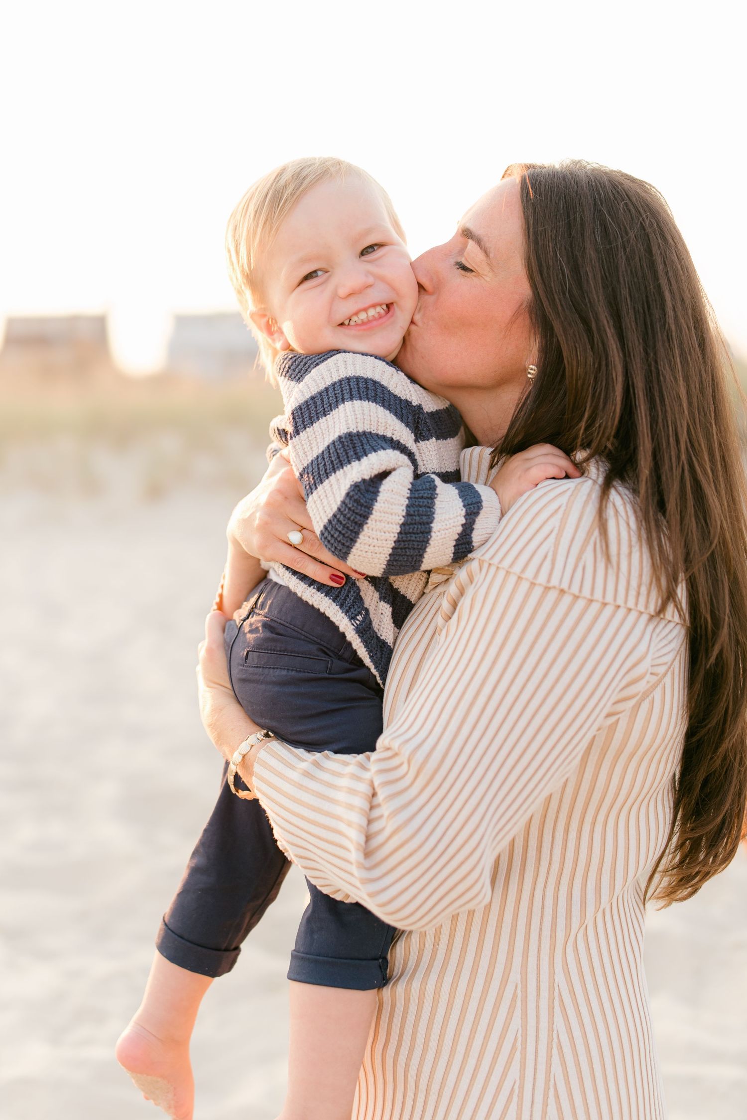 a mother in a beige dress kisses her son on the cheek while Lauren Marie photography captures the moment.