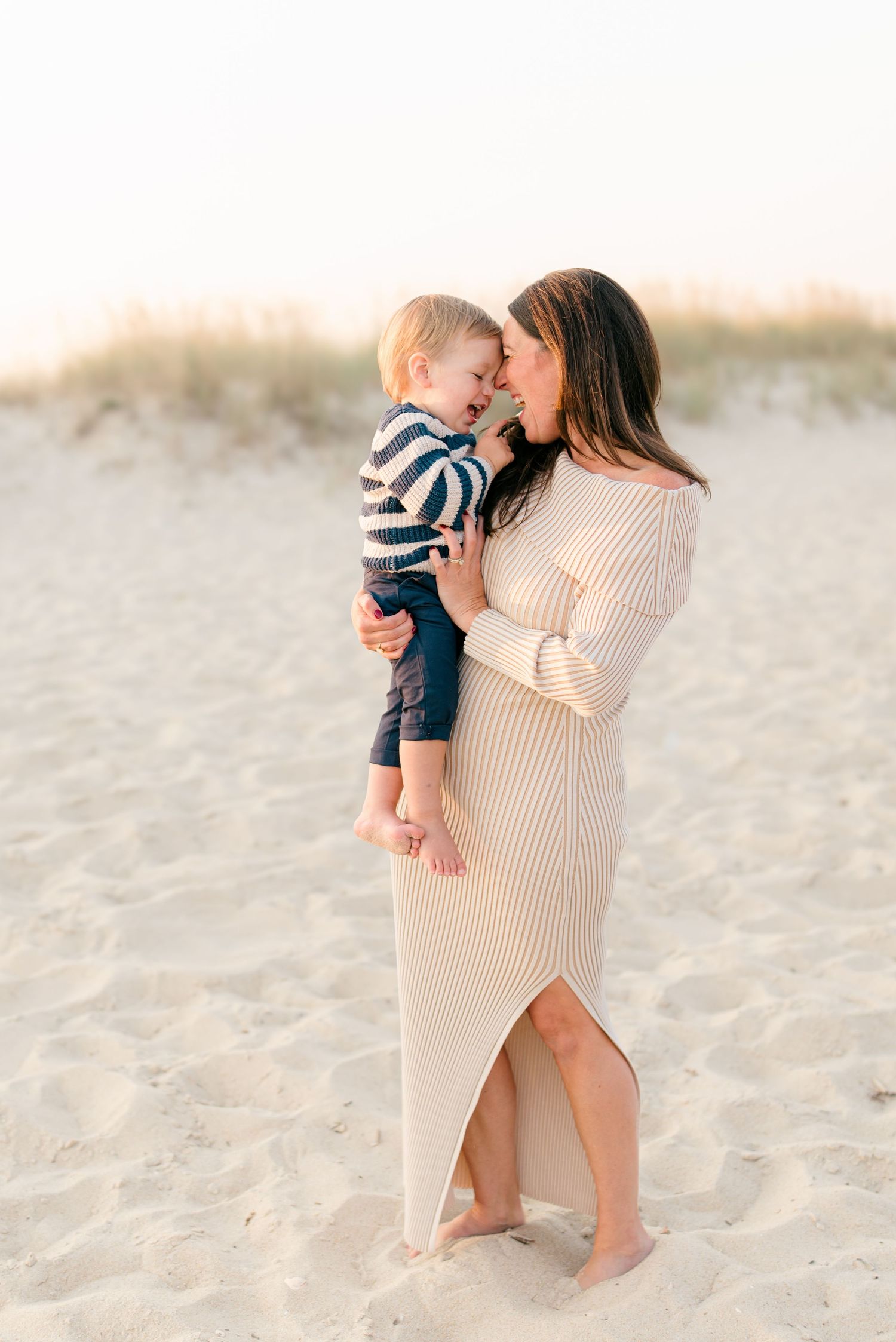 A mother holds her son with foreheads touching in front of the dunes on the spring lake beach.