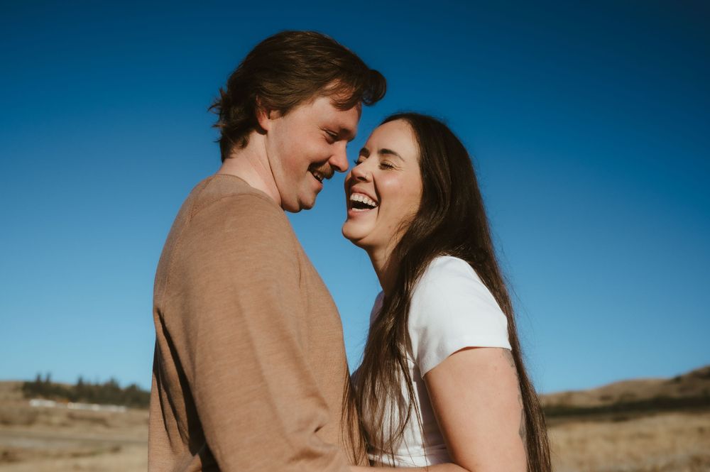 Couple laughing together against bright blue sky in outdoor natural setting.