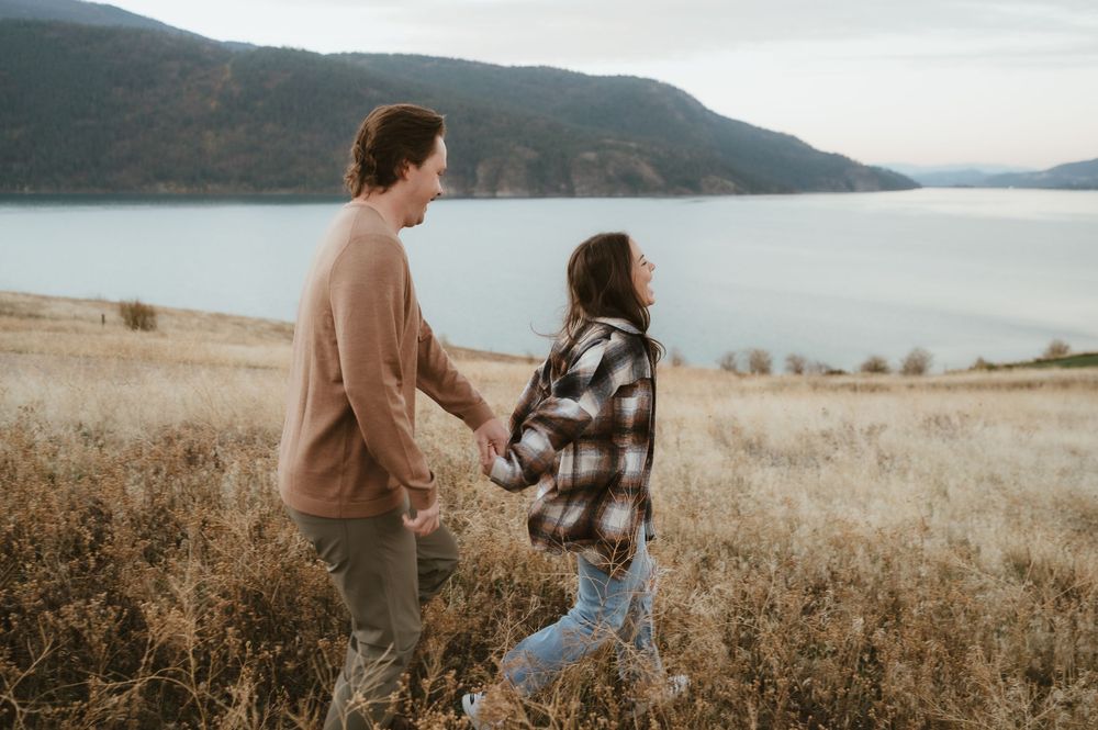 Couple walking through autumn field with scenic mountain lake in background.