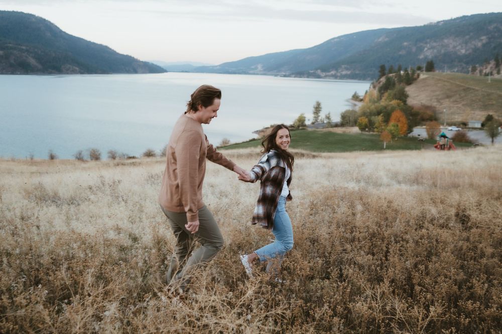 Playful couple dancing in field overlooking pristine mountain lake.