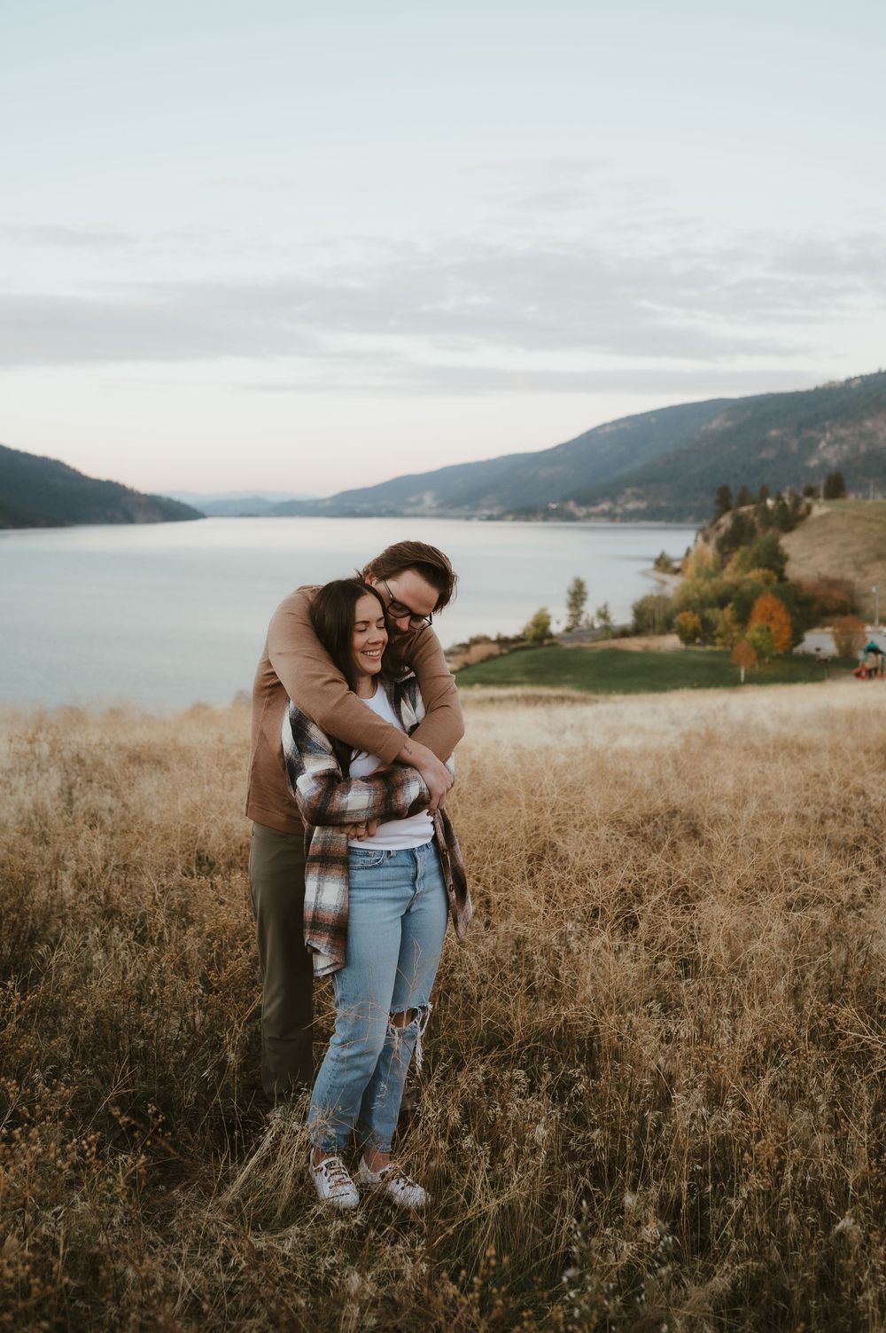 Loving embrace captured against serene lake and mountain backdrop at sunset.