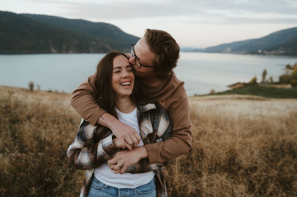 Couple in casual attire embracing and laughing in scenic mountain landscape.