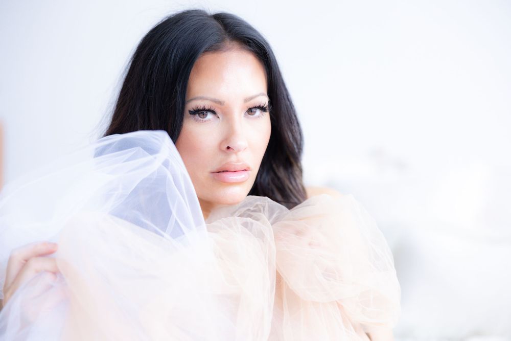 A stunning dark-haired woman poses confidently wrapped in sheer pink tulle in a bright, airy setting.