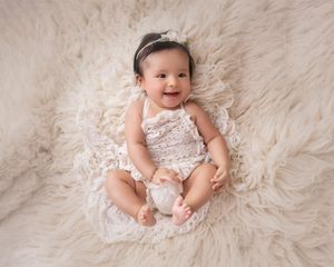 Young baby wearing delicate lace outfit posed on soft cream-colored fur backdrop.