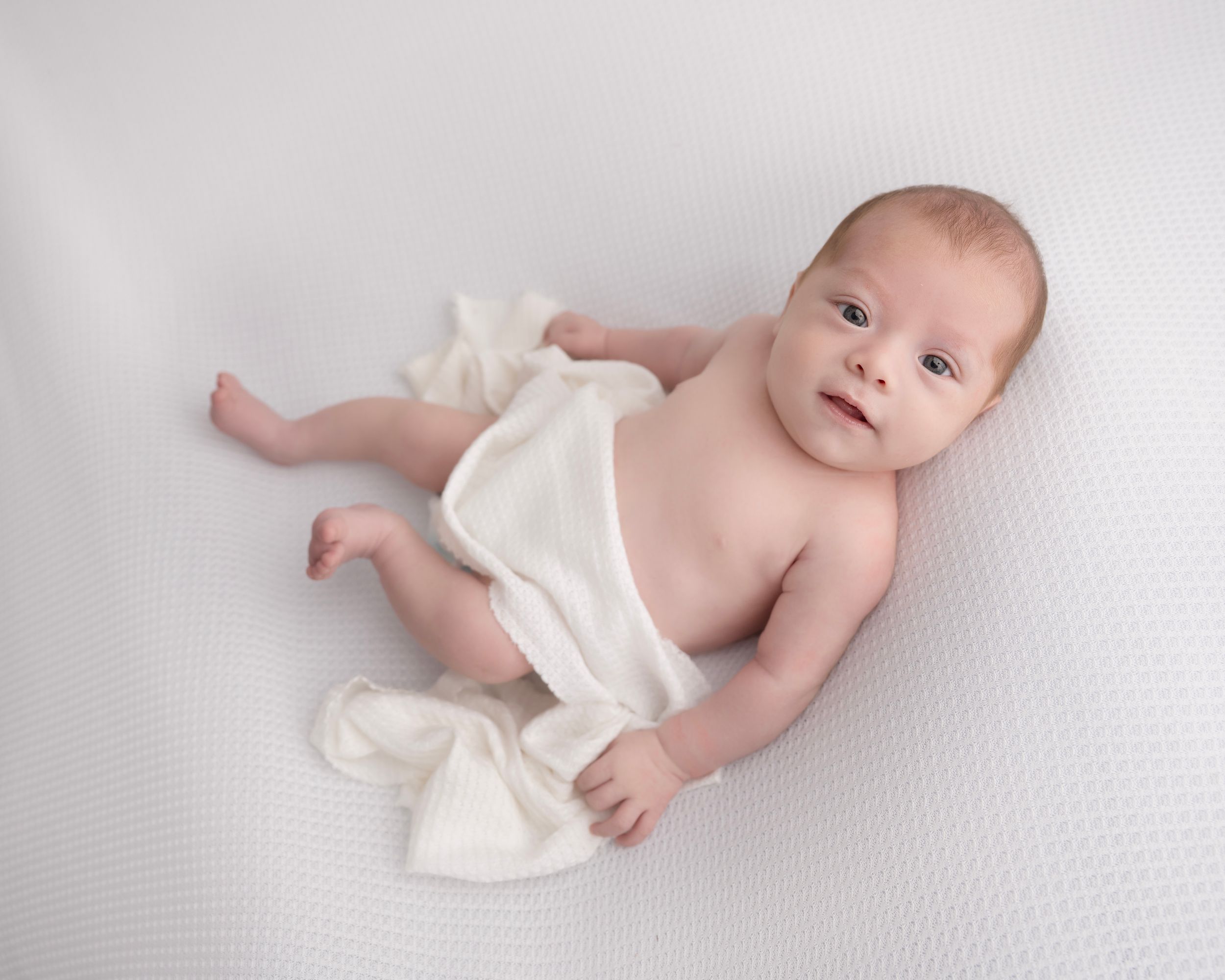 Minimalist baby photography session on white textured backdrop showing natural poses.