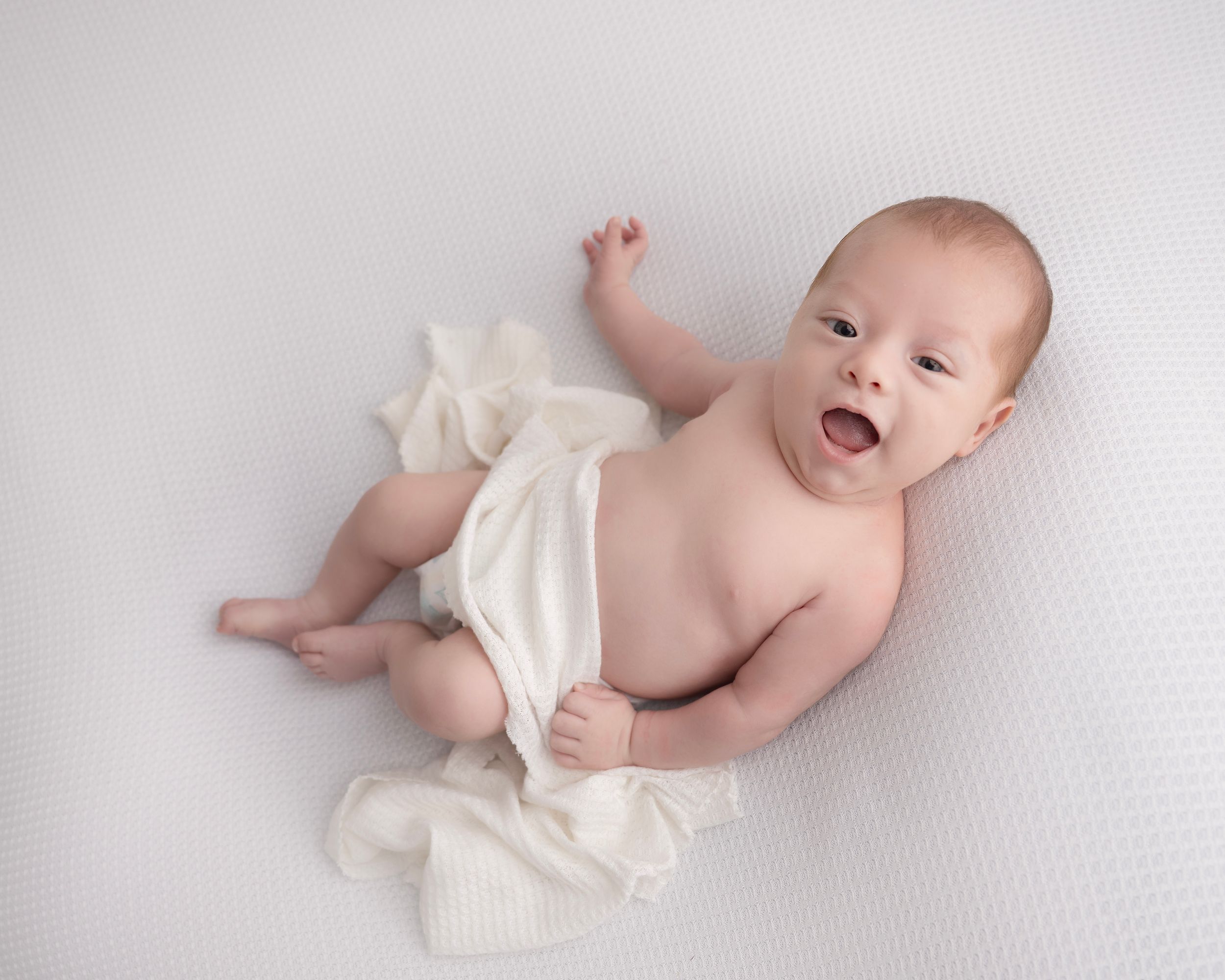 Sweet baby wearing white diaper photographed on soft white background.