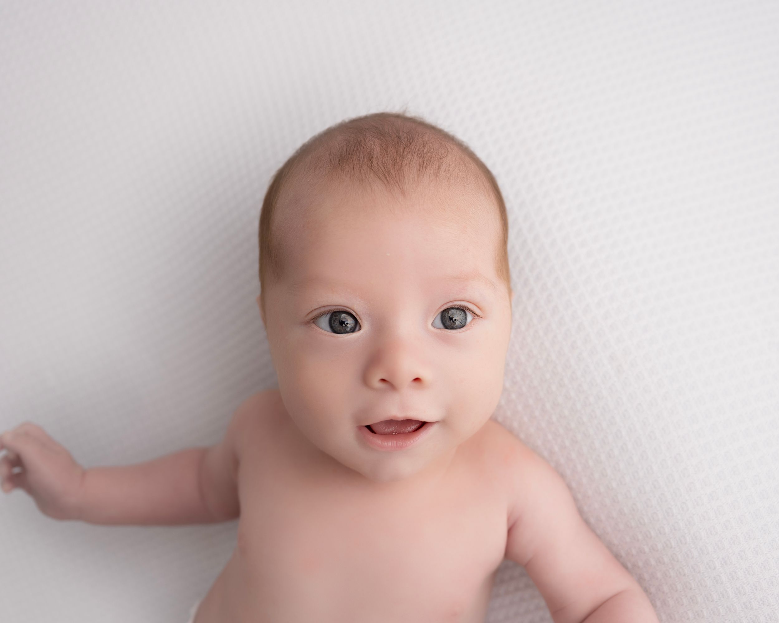 Professional newborn photography series featuring a baby lying on white textured backdrop.