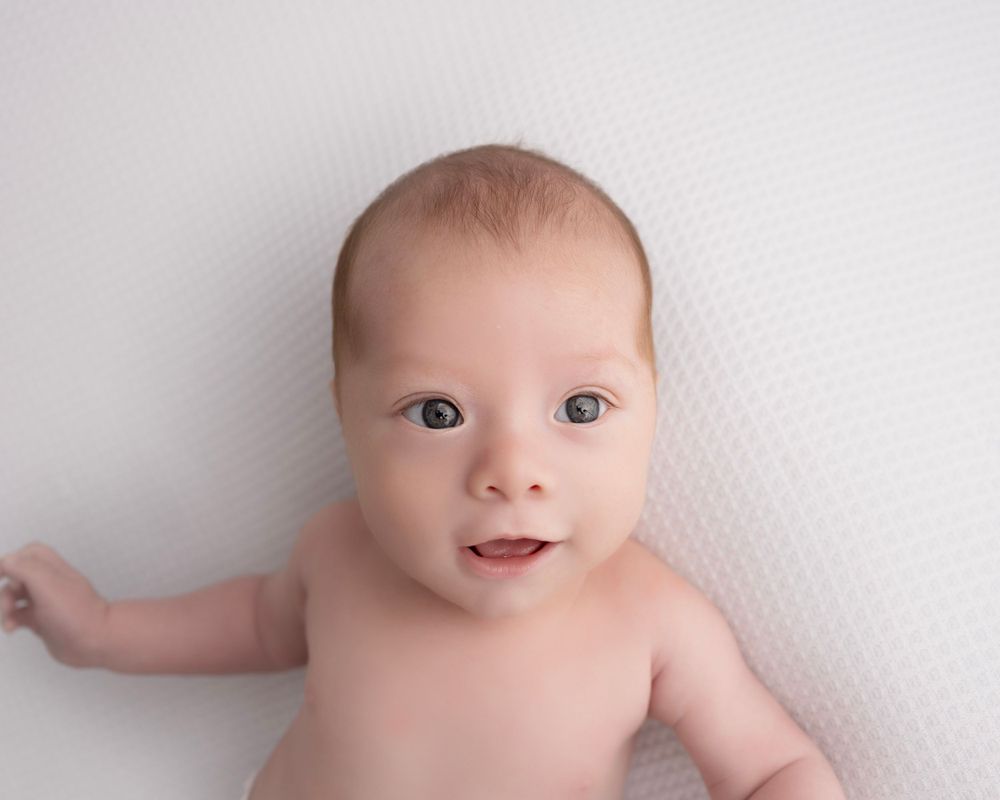 Professional newborn photography series featuring a baby lying on white textured backdrop.