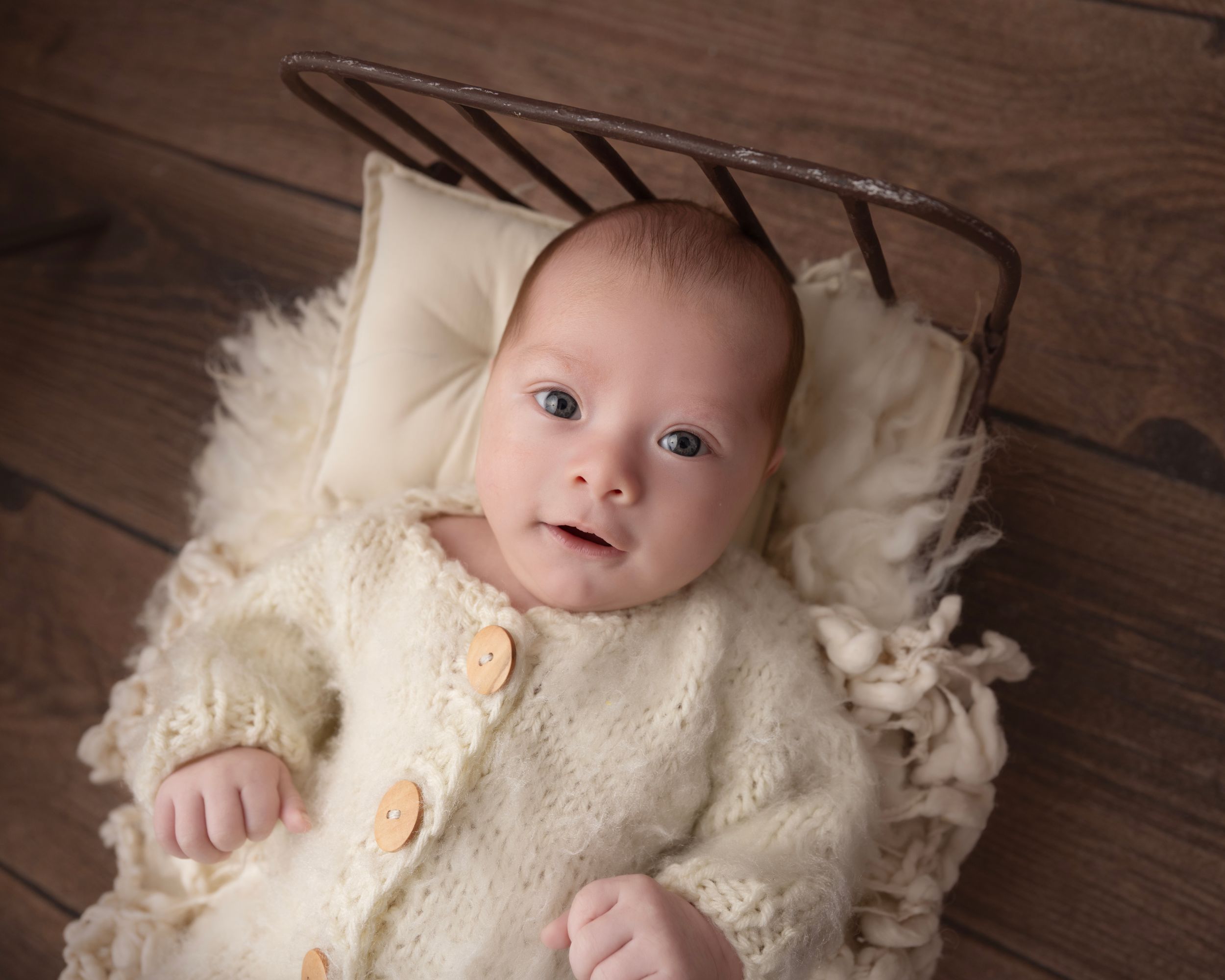 Artistic newborn photography on rustic wooden floor with vintage cream textiles.