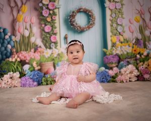 Spring photo setup with blue door, floral wreath, pink tulips, and butterfly decorations in pastel colors.