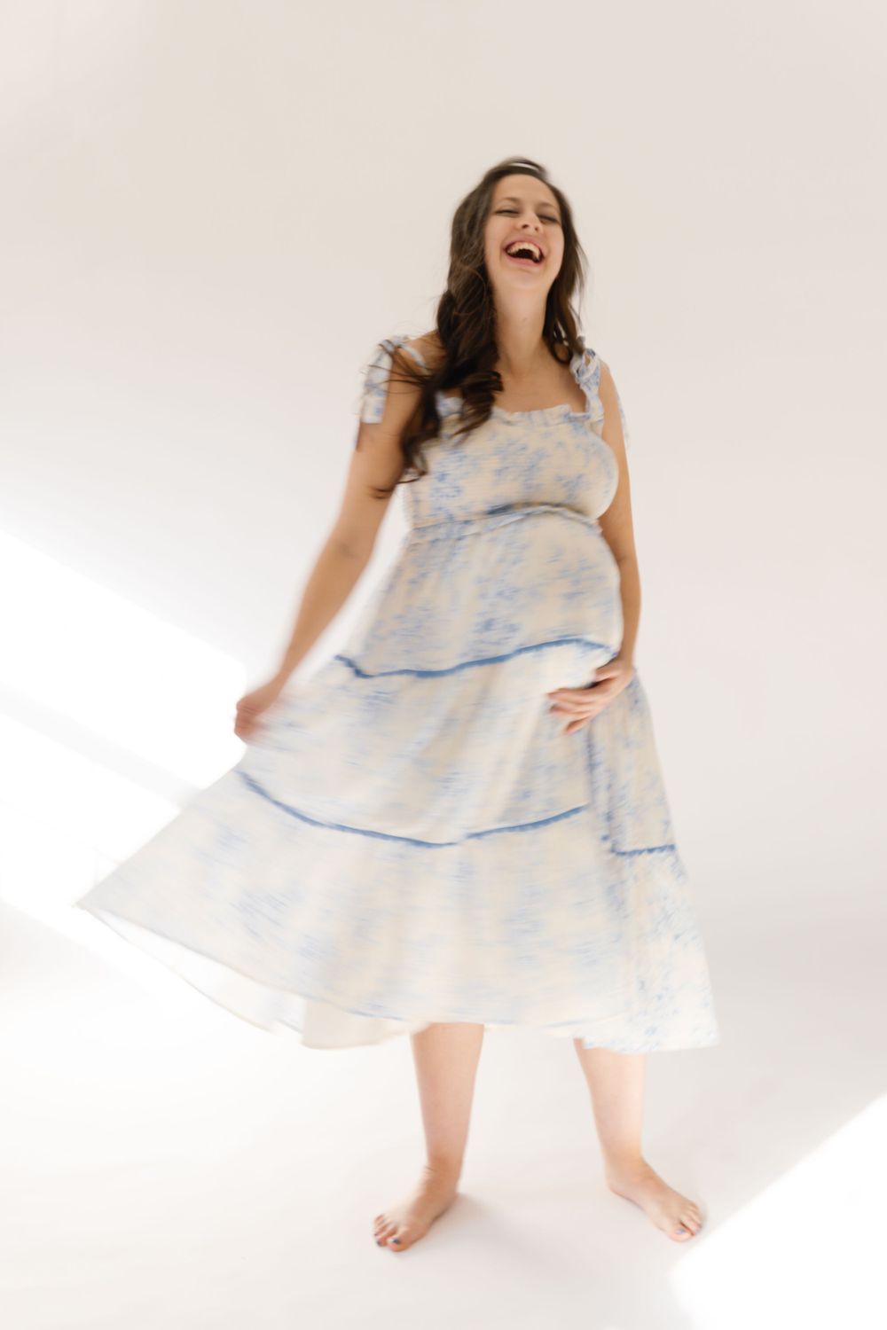 Someone wearing a flowing white dress with blue stripes twirls joyfully barefoot against a light background.