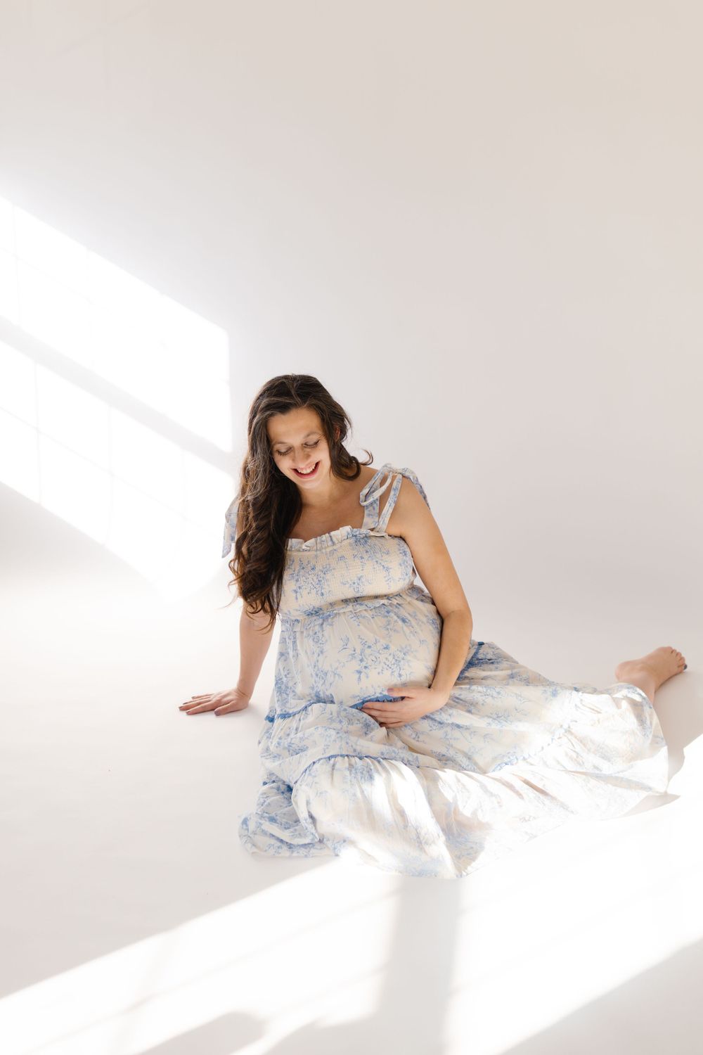 A woman in a floral dress sits on the floor in bright sunlight streaming through a window.