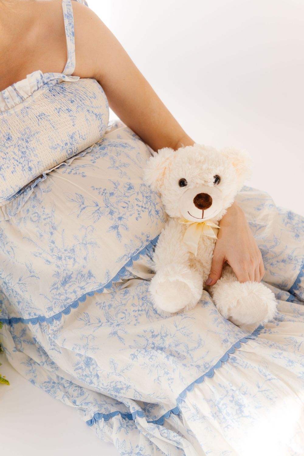 White teddy bear with yellow bow rests against a person wearing blue and white floral maternity dress.