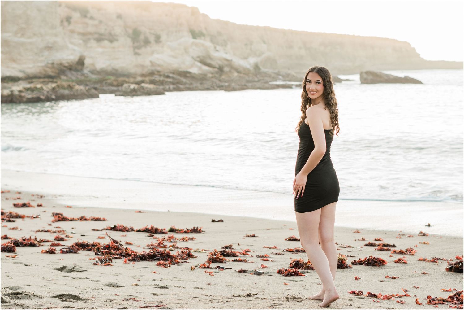 san luis obispo high school senior portraits in black dress standing on beach with cliff in the background