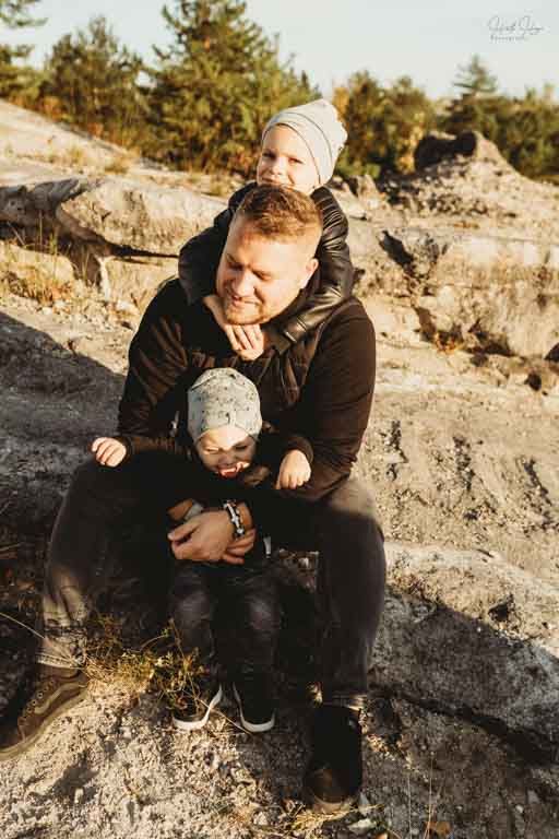 A parent and children sitting together on rocky terrain during a sunny day in an outdoor natural setting.