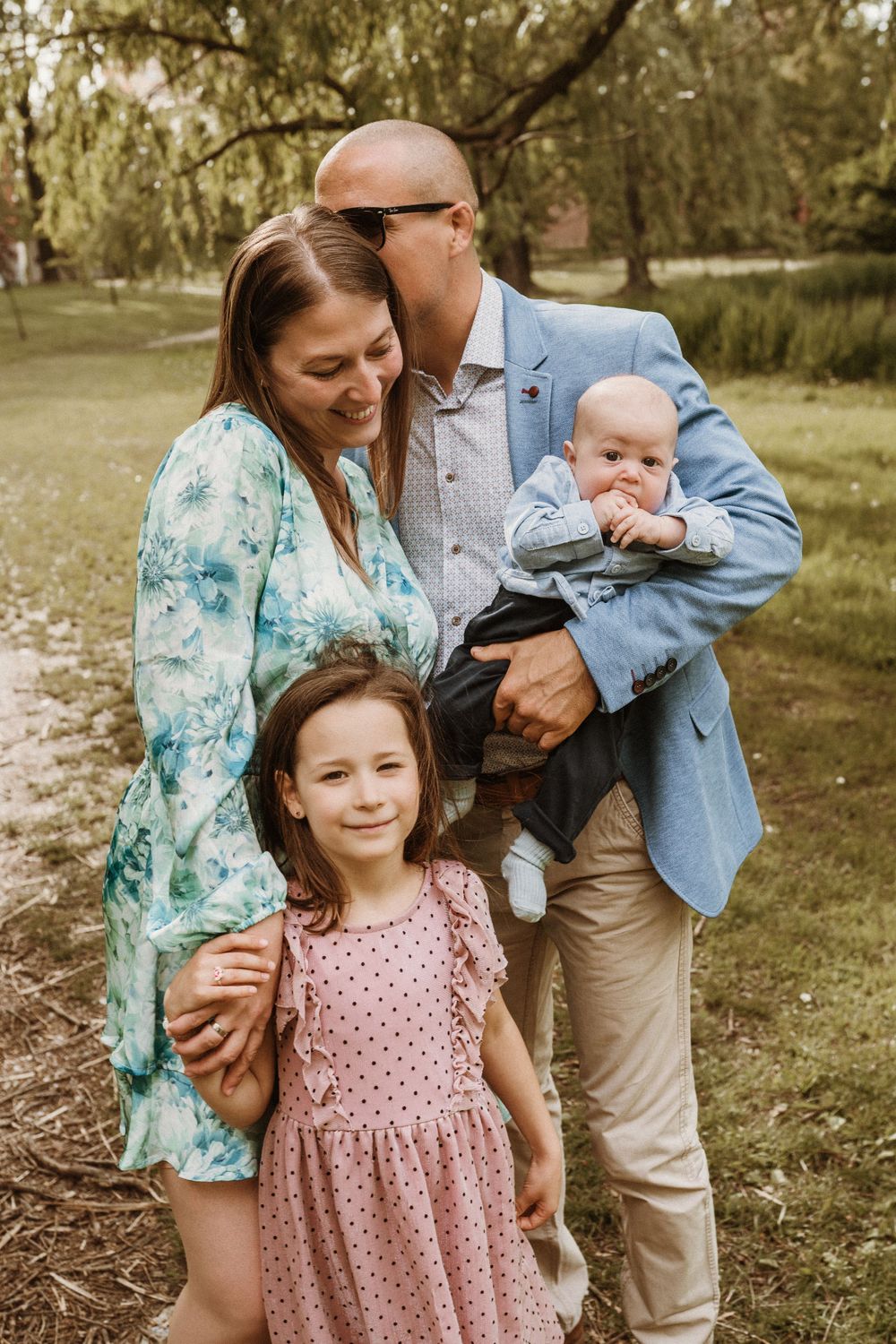 A happy family posing together outdoors on a sunny day, wearing spring attire in a natural park setting.